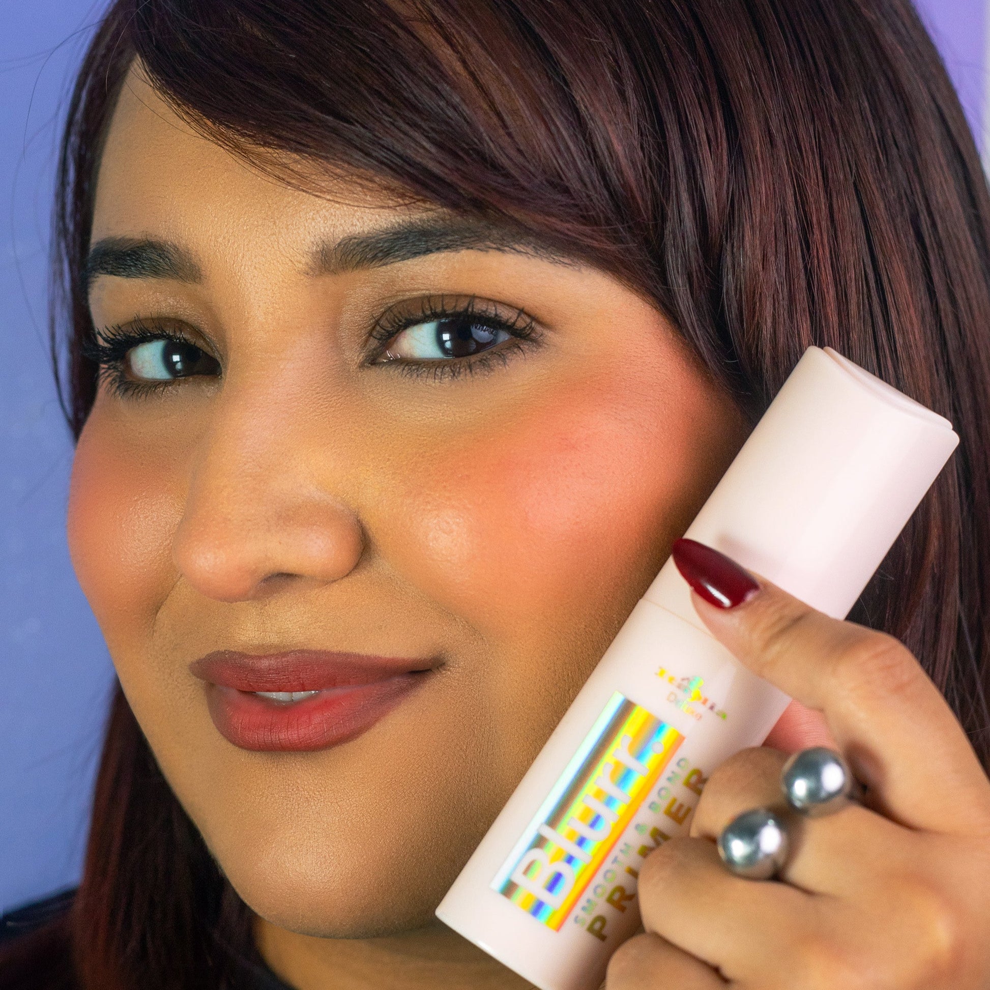 Hand holding a bottle of 'Blur Smooth & Blend Primer' with a light blue background