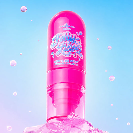 A bright pink cylindrical cosmetic bottle labeled 'JELLYLICIOUS Grip and Set Spray" emerging from a block of ice against a soft blue gradient background with floating jelly.