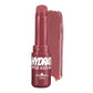 A tube of Italia Deluxe Hydrahit Peptide Gloss Balm in a deep berry pink shade, shown with a glossy smear of the product behind it on a white background.