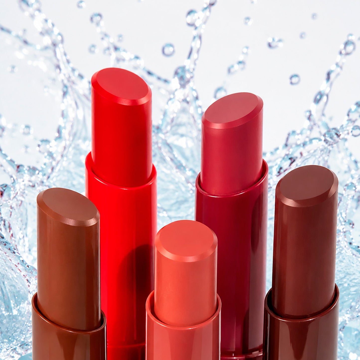 Five lipstick tubes in a gradient of warm and cool reds, browns, and coral, arranged against a dynamic water splash background.