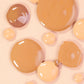 Close-up foundation swatches in a range of skin tones, showing a smooth, blendable, soft matte texture.